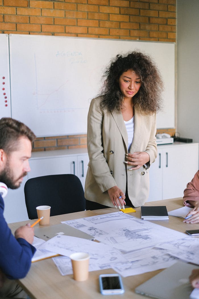 Concentrated female in elegant clothes standing at table with papers while working with coworkers during brainstorm in modern coworking space